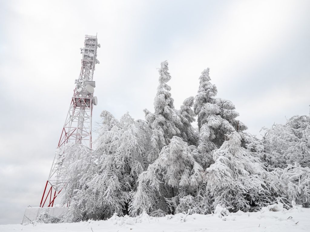 A telecommunications tower beside snow-covered trees, showing how frost and ice can affect signal transmission while modern technology continues to provide connectivity in extreme winter conditions.