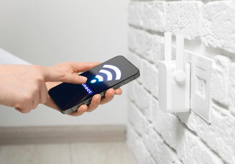 Woman with smartphone connecting to internet via wireless repeater indoors, closeup. Wi-Fi symbol on device screen in Menomonie, Wisconsin